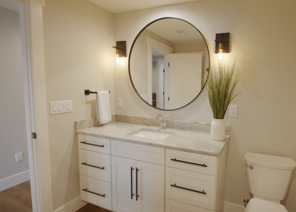 Parade of Homes 2022's guest bathroom with round mirror and light fixtures