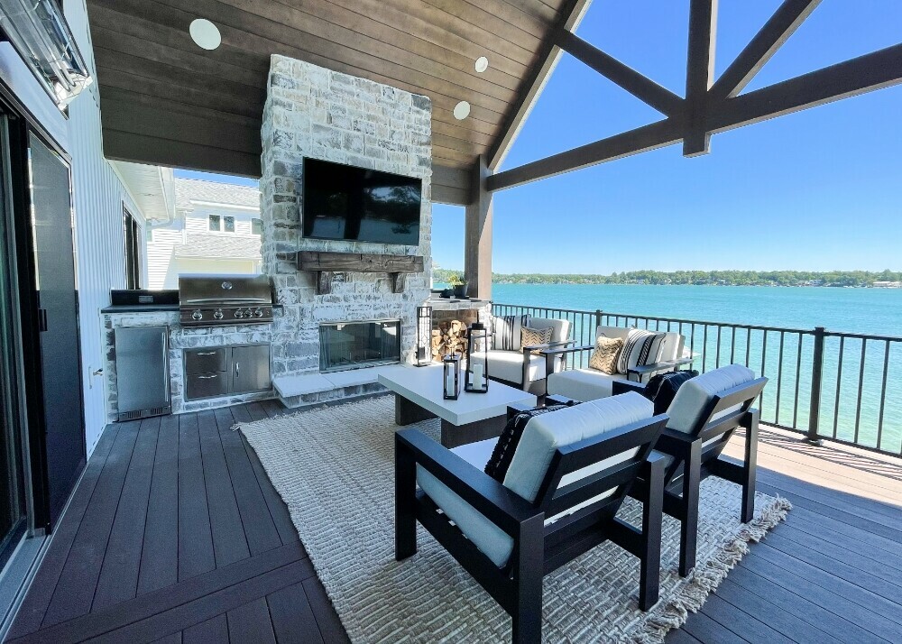 Parade of Homes 2022's custom exterior fireplace with a built-in grill and lounge seating overlooking the blue lake