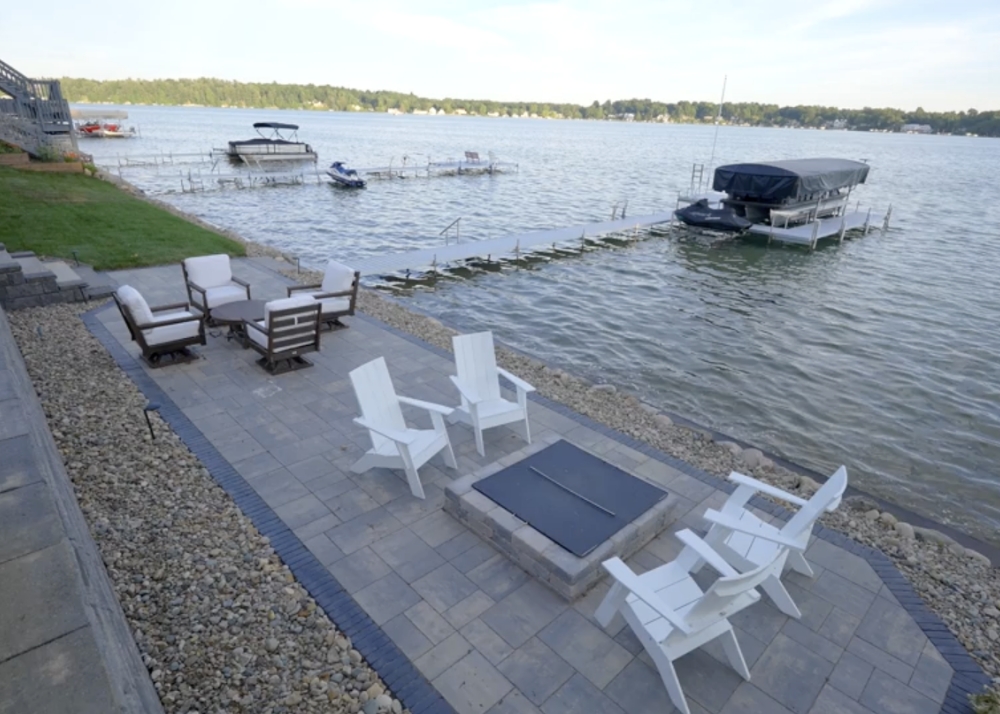 Parade of Homes 2022's outdoor lounge chairs and build-in fireplace next to the lake and dock